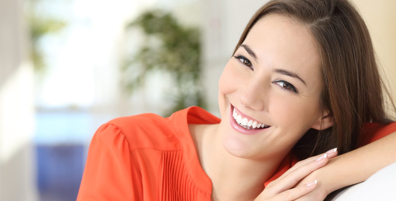 Angstpatienten 52549287 - beauty woman with perfect white teeth and smile wearing an orange blouse looking at camera sitting on a couch at home